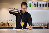 Smiling bartender pouring yellow cocktail into glass