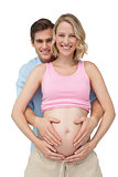 Expectant happy parents making a heart shape on mothers baby bump