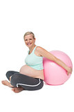 Happy pregnant woman leaning against pink exercise ball