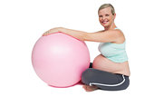 Smiling pregnant woman leaning against pink exercise ball