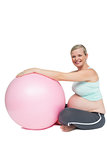 Cheerful pregnant woman leaning against pink exercise ball