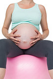 Pregnant woman sitting on pink exercise ball holding her belly