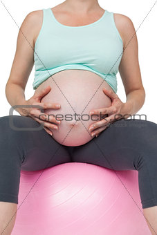 Pregnant woman sitting on pink exercise ball holding her belly