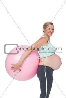 Happy pregnant woman holding pink exercise ball behind her back