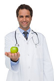Happy doctor smiling and holding apple to camera