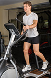 young man does workout at elliptical trainer in gym
