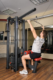 Young man doing lats pull-down workout in gym