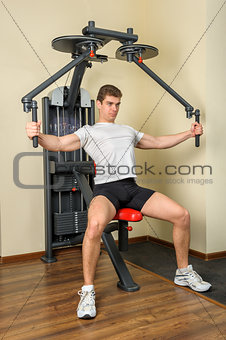 young man does workout at chest fly machine in gym
