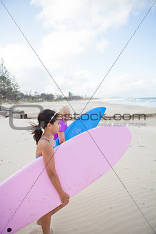 Two cute young girls walking together with surfboards at beach