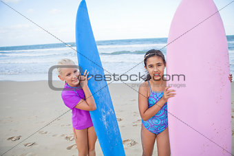 Two happy young girls holding surfboards at beach