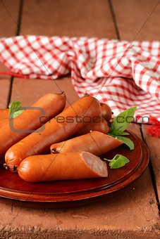 delicious smoked sausages on a wooden plate with basil leaves