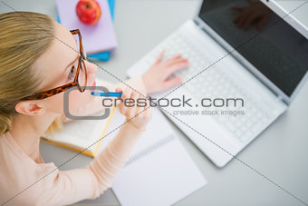 Thoughtful young woman studying in kitchen
