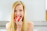 Happy young woman eating apple in kitchen