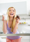 Happy young woman with milk and chocolate muffin in kitchen