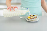 Closeup on young woman pouring milk into muesli