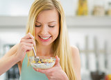 Happy young woman eating muesli in kitchen