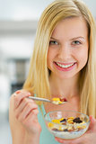 Portrait of happy young woman eating muesli in kitchen