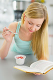 Young woman eating yogurt and reading book