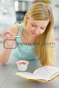 Young woman eating yogurt and reading book