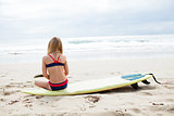 Young girl sitting on surfboard on beach