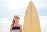 Smiling young girl standing next to surfboard