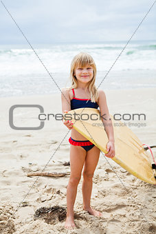 Smiling young girl holding surfboard on beach