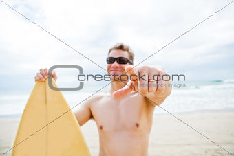 Smiling man with surfboard at beach pointing with finger