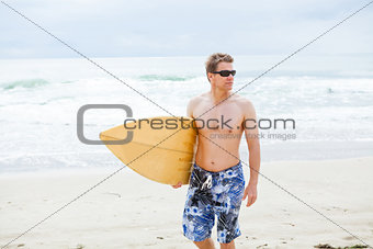 Serious looking man walking with surfboard at beach
