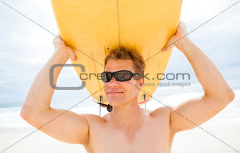 Smiling man resting surfboard on head at beach
