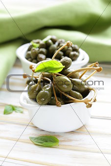 two kinds of pickled capers in white bowl on wooden table