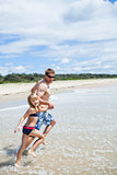 Happy father and daughter running along beach in shallow water