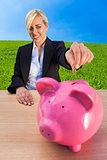 Woman Putting Money into Pink Piggy Bank