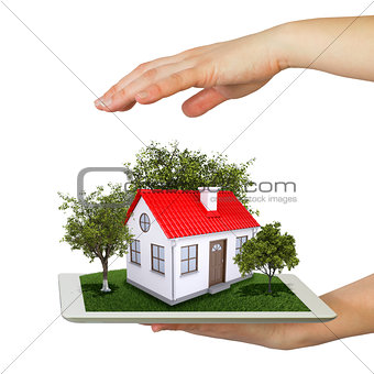 Hands holding tablet pc and small house with land