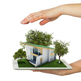 Hands holding tablet pc and small house with land