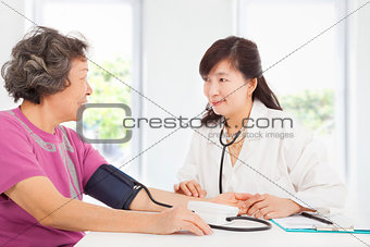 doctor measuring blood pressure of senior woman at home