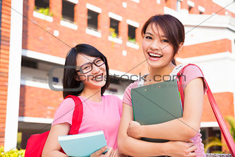 two smiling students holding books  at campus