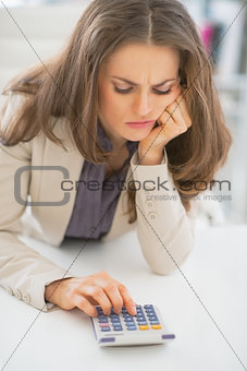 Frustrated business woman sitting in office and using calculator