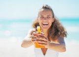 Closeup on young woman pointing bottle of sun block creme in cam