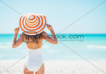Young woman in hat standing on beach. rear view