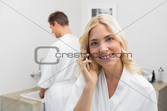 Woman using cellphone with man in background in kitchen
