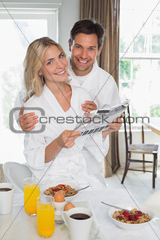 Happy couple reading newspaper while having breakfast at home