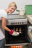 Smiling woman putting a tray of cookies in oven at kitchen