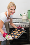 Smiling woman putting a tray of cookies in oven