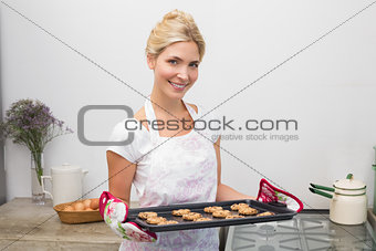 Smiling young woman holding a tray of cookies in kitchen