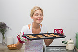 Woman holding a tray of cookies with eyes closed in kitchen