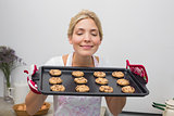 Woman holding a tray of cookies with eyes closed in kitchen