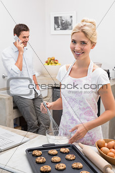 Woman preparing cookies while man on call in the kitchen
