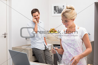 Smiling woman preparing cookies while man on call in kitchen