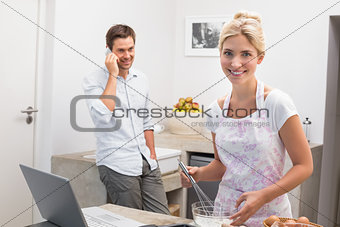 Woman preparing cookies while man on call in kitchen