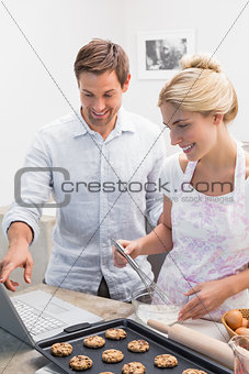 Couple preparing cookies while using laptop in the kitchen